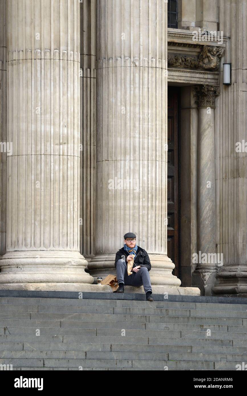 Londra, Inghilterra, Regno Unito. Uomo che mangia il suo pranzo sui gradini della Cattedrale di San Paolo curando il secondo blocco COVID, novembre 2020. Foto Stock