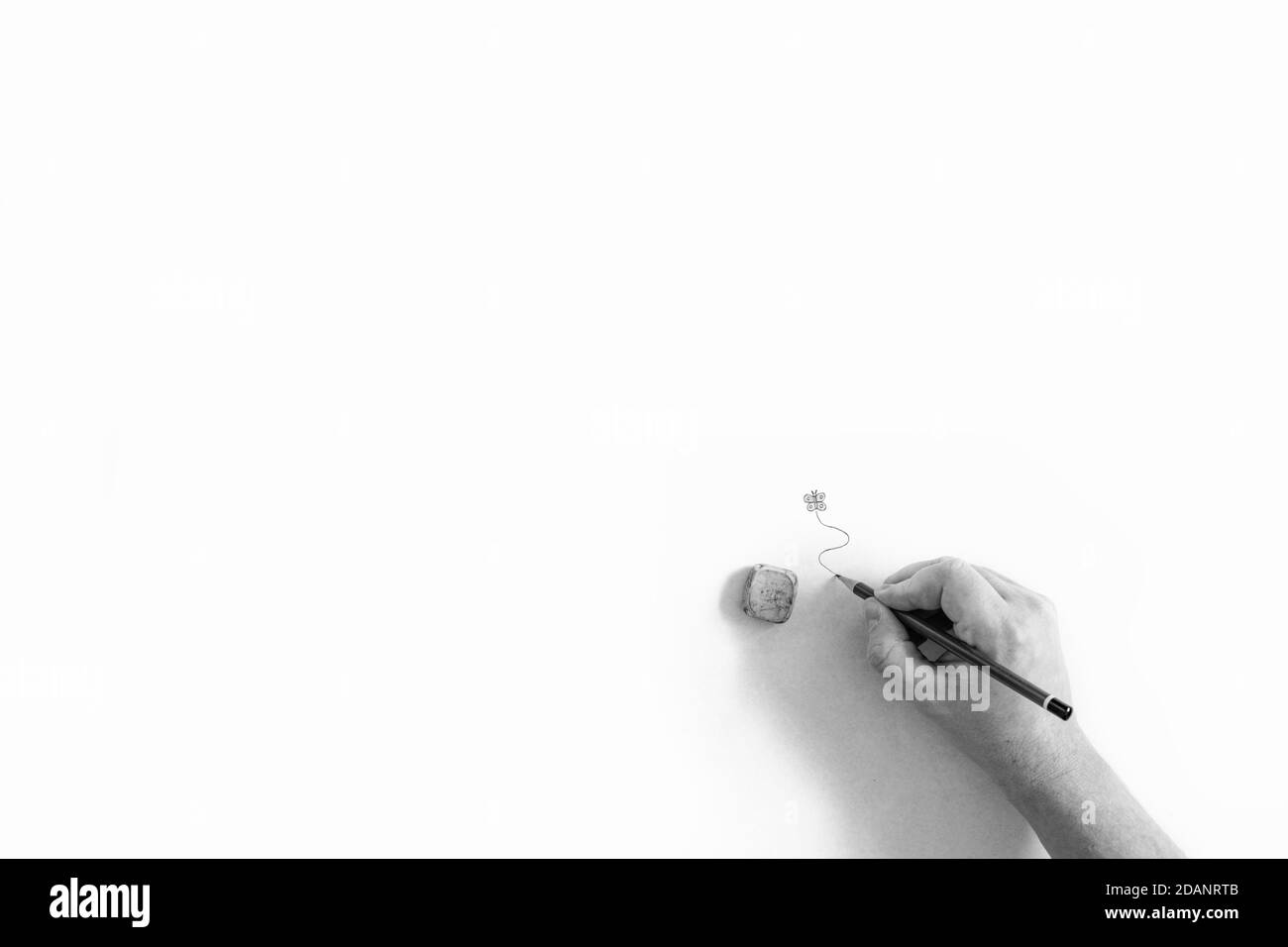 Un ritratto astratto in bianco e nero minimalista di una mano di una persona che tiene una matita, disegnando una linea vorticosa sotto una farfalla disegnata. Foto Stock