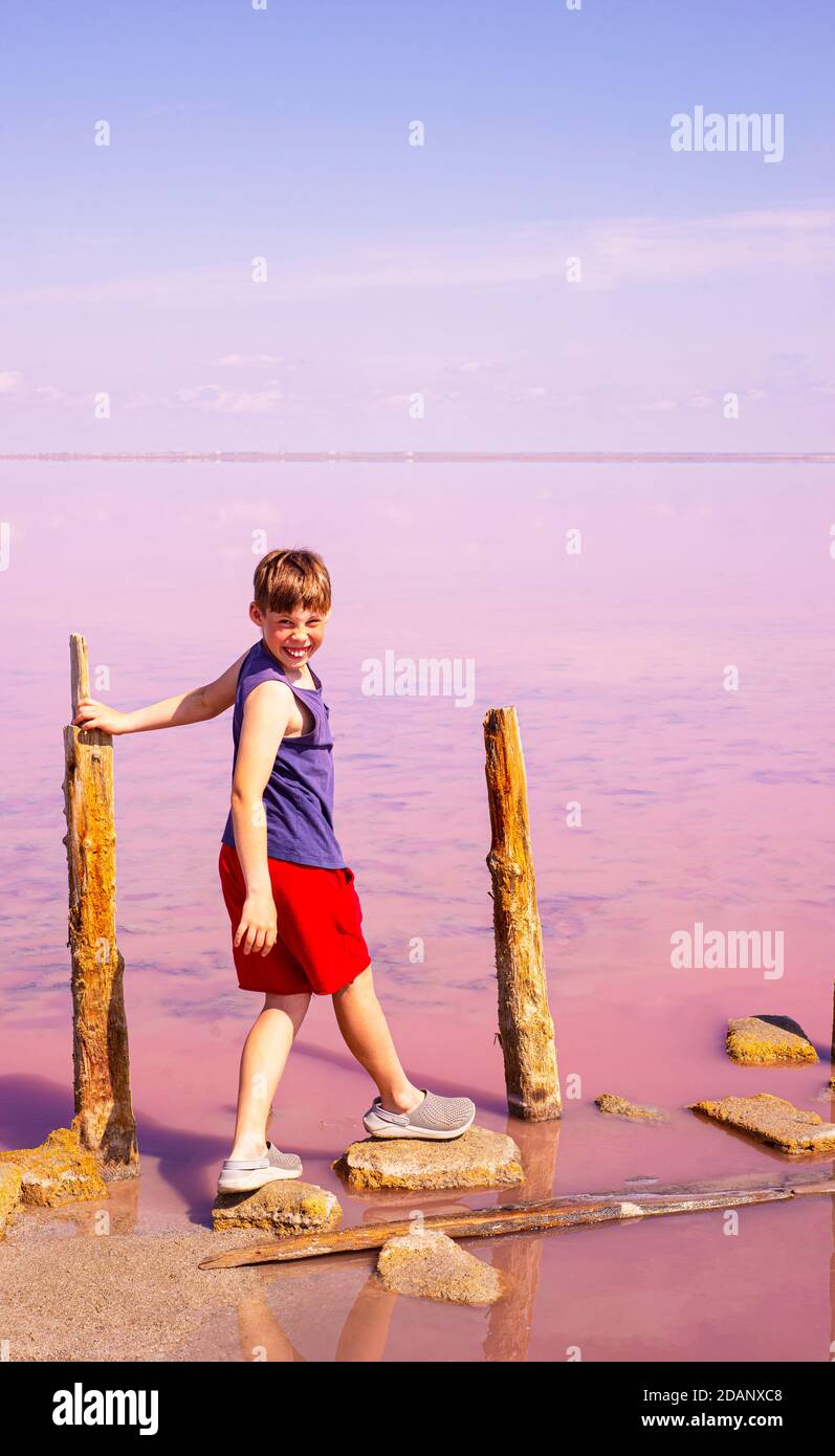 Entra nell'ignoto con un sorriso e una speranza. Un ragazzo scala su pietre su un lago da favola rosa. Foto concettuale. L'idea di ​​faith in un futuro migliore Foto Stock