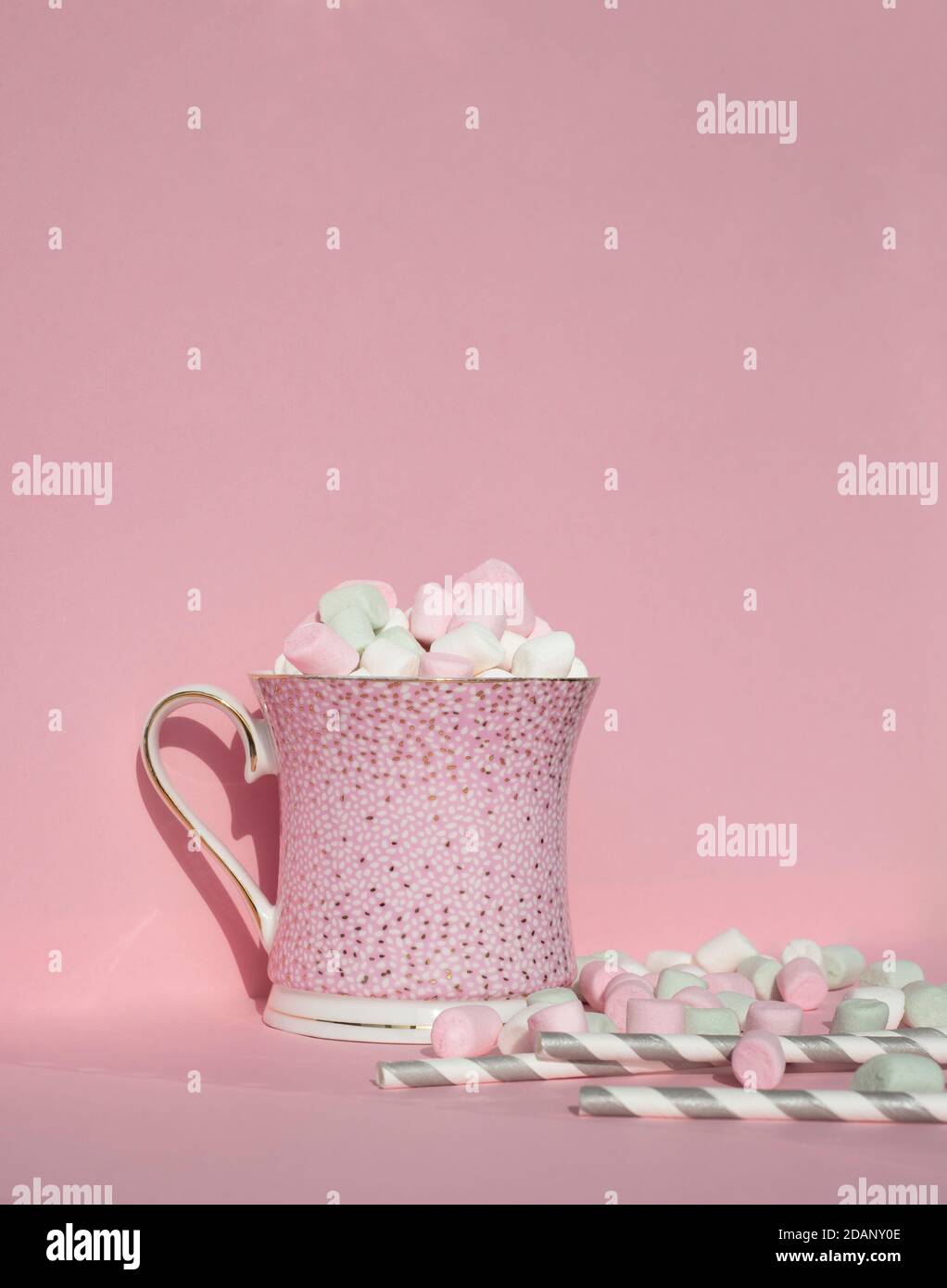 Tazza con cacao caldo e marshmallows sulla parte superiore. Bevanda calda festiva sfondo rosa. Tazza rosa. Carino cannucce di carta per bevande e teneri cubetti di marshmallow. Foto Stock