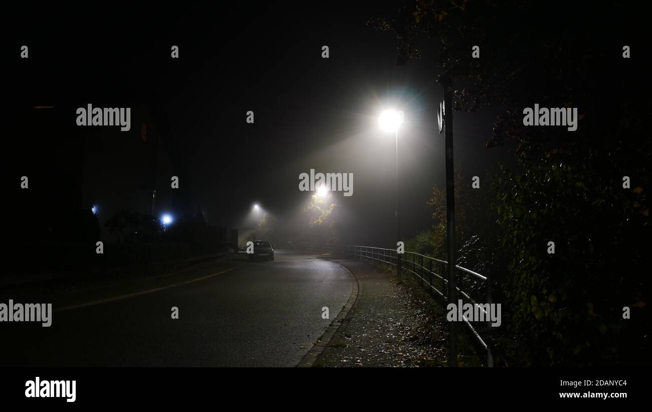 Dark foggy città strada a novembre con luci di strada che illuminano dare una sensazione di solitudine nei tempi della corona pandemia Foto Stock