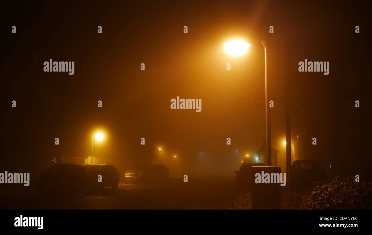 Piccolo villaggio durante una notte di autunno foggy in novembre con Nebbie sulla strada e luci di strada incandescenti durante la Corona pandemia Foto Stock