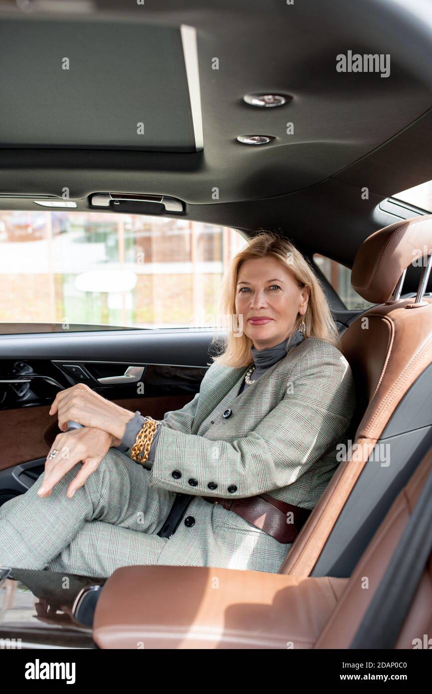Donna d'affari graziosa che lo guarda con il sorriso mentre sedendosi sopra sedile posteriore dell'auto Foto Stock