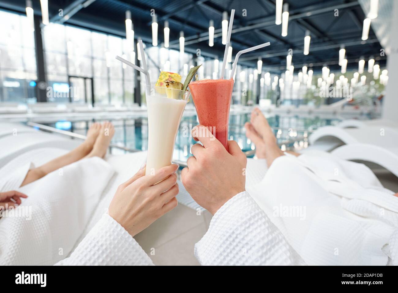 Mani di giovane coppia riposante in accappatoi bianchi che si accoppiano con cocktail Foto Stock