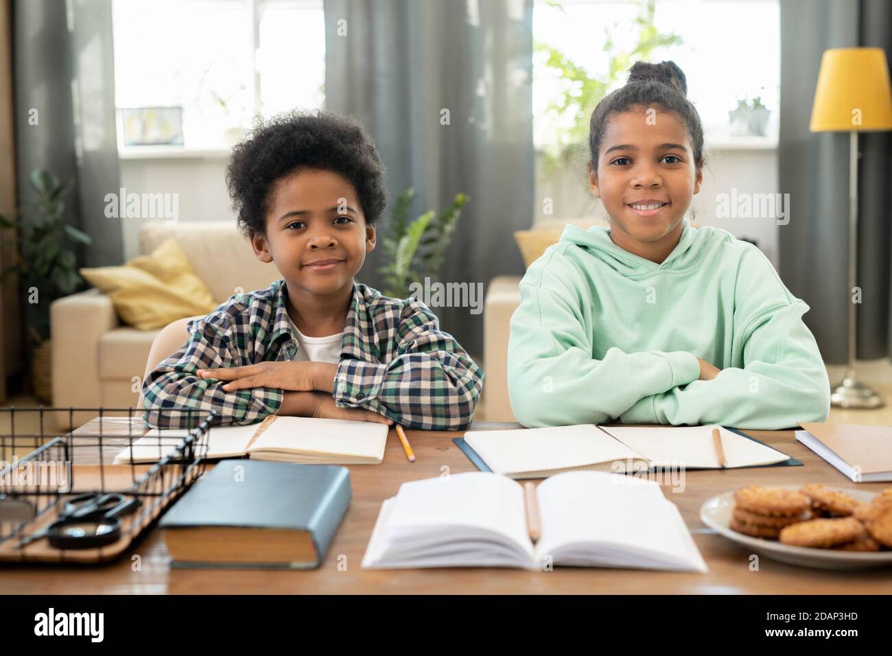 Felice ragazza elementare e ragazzo in casualwear seduto al tavolo in soggiorno Foto Stock
