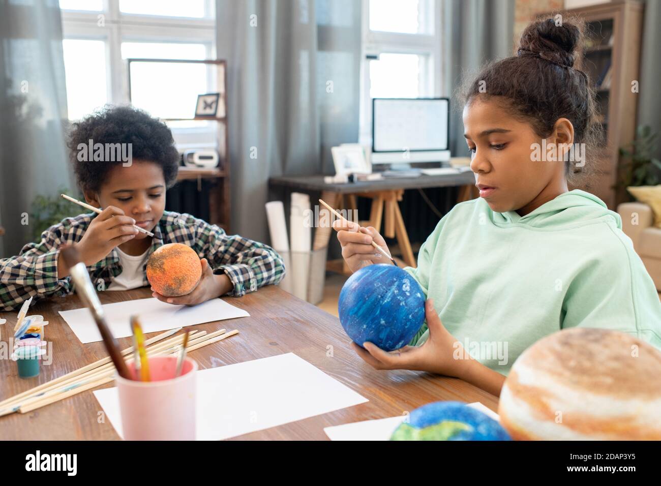 Due adorabili fratelli di razza mista in casualwear pittura pianeti da tavolo a casa Foto Stock