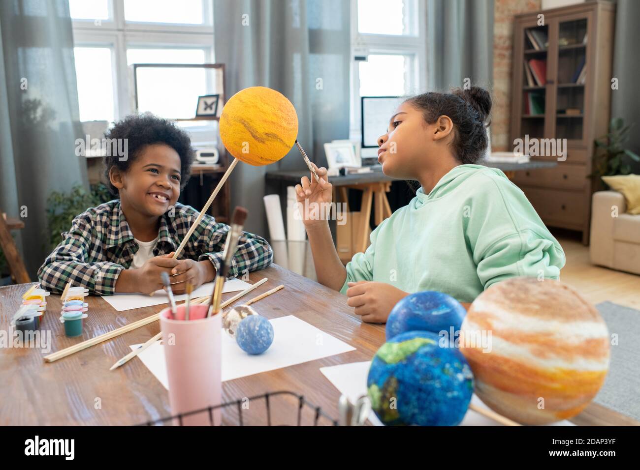 Due adorabili studenti di razza mista in casualwear pittura pianeti per tavolo Foto Stock