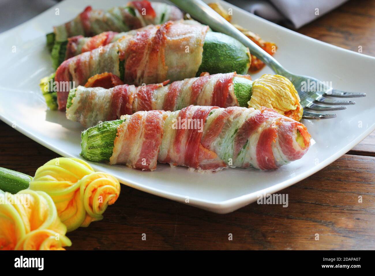 Patatine grigliate di zucchine avvolte in una pancetta su un piatto bianco Foto Stock