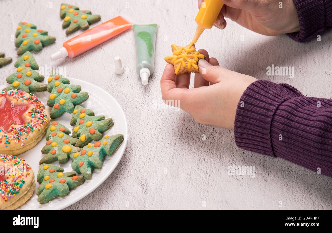 Le mani delle donne dipingono pan di zenzero di Natale. Preparazione per la celebrazione del Natale e del Capodanno. Orientamento orizzontale. Foto Stock