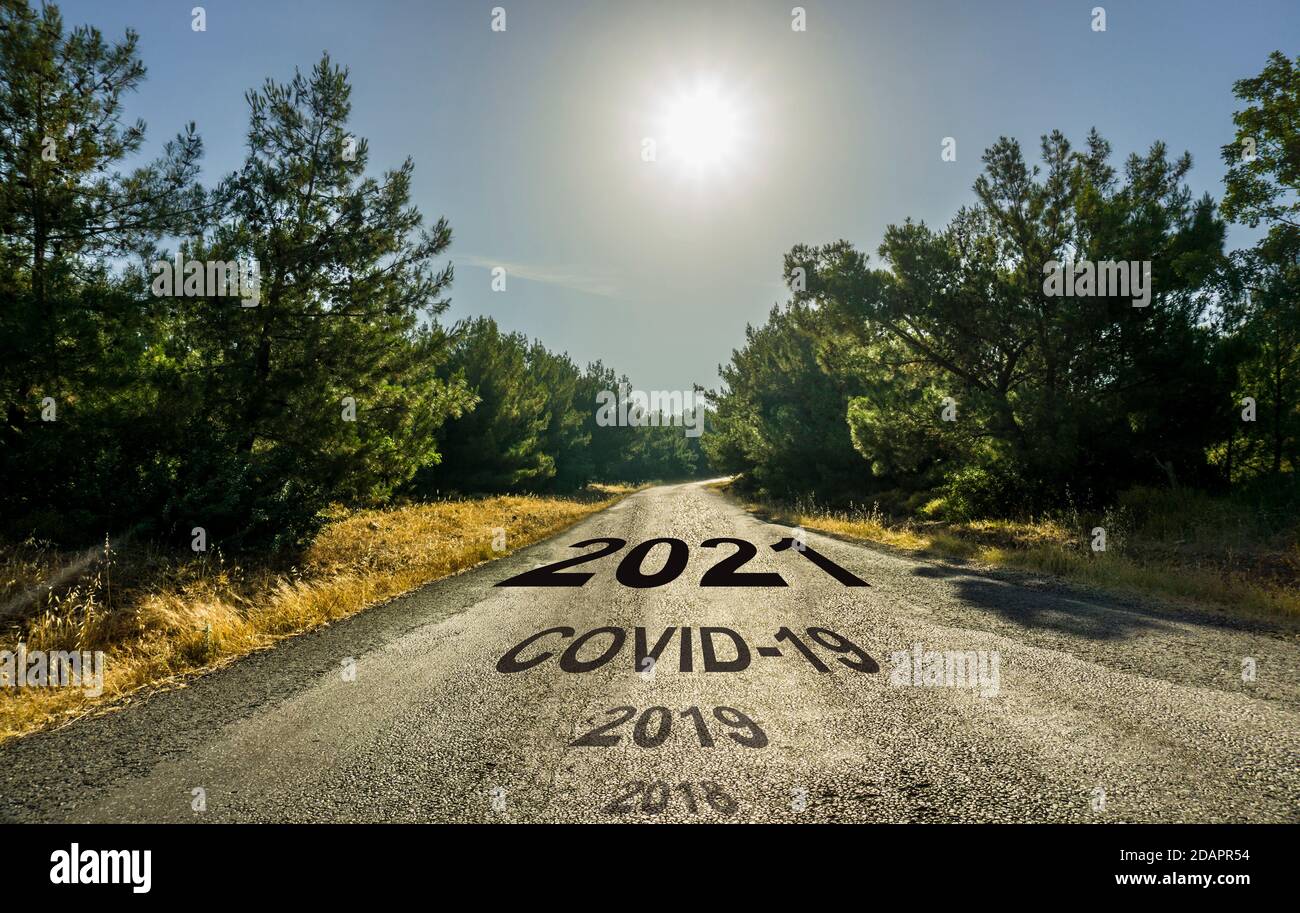 Felice anno nuovo 2021 concetto. Strada asfaltata in foresta. Il sole splende su una strada vuota in campagna che conduce a lontano attraverso gli alberi in primavera o in autunno. Foto Stock