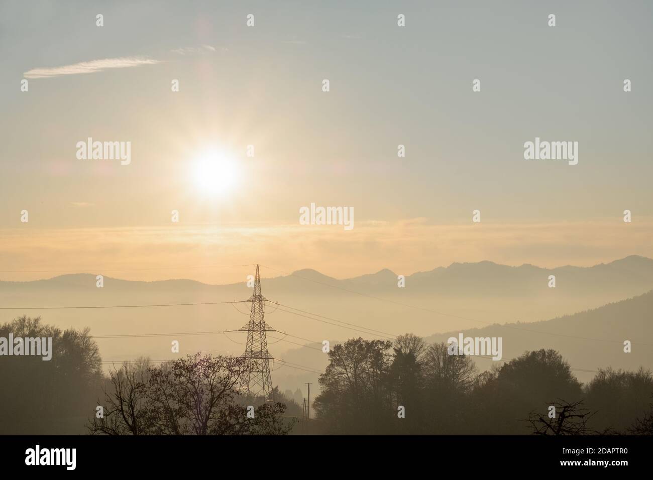vista delle infrastrutture elettriche, dei poli elettrici e dei cavi in un bellissimo paesaggio con montagne nebbie e il sole che tramonta. Foto Stock
