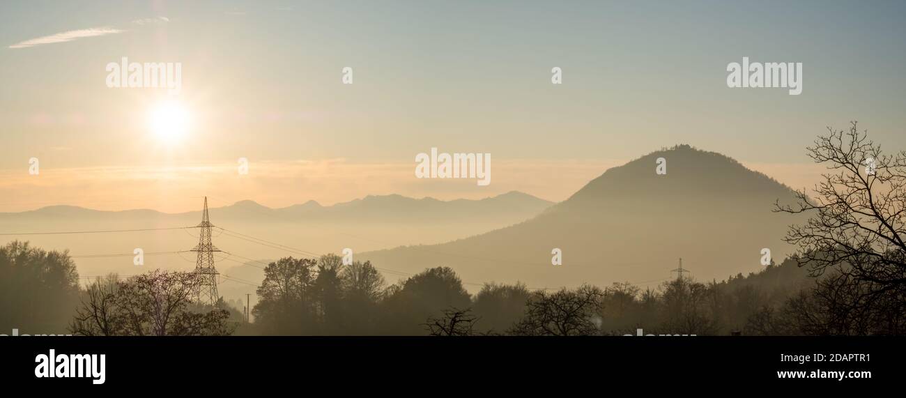 vista delle infrastrutture elettriche, dei poli elettrici e dei cavi in un bellissimo paesaggio con montagne nebbie e il sole che tramonta. Foto Stock