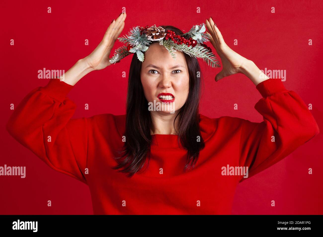 Primo piano ritratto di una giovane asiatica nervosa e aggressiva in una corona di Natale con le mani che la tengono in testa Foto Stock