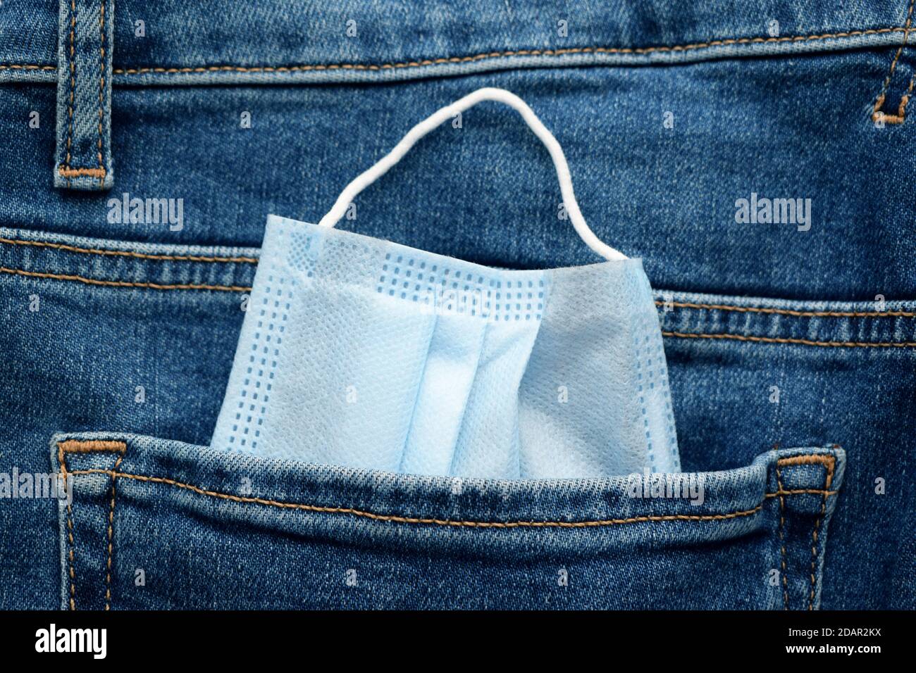 Tasca jeans con maschera medica usa e getta blu primo piano. Equipaggiamento protettivo quotidiano contro l'infezione da coronavirus Foto Stock