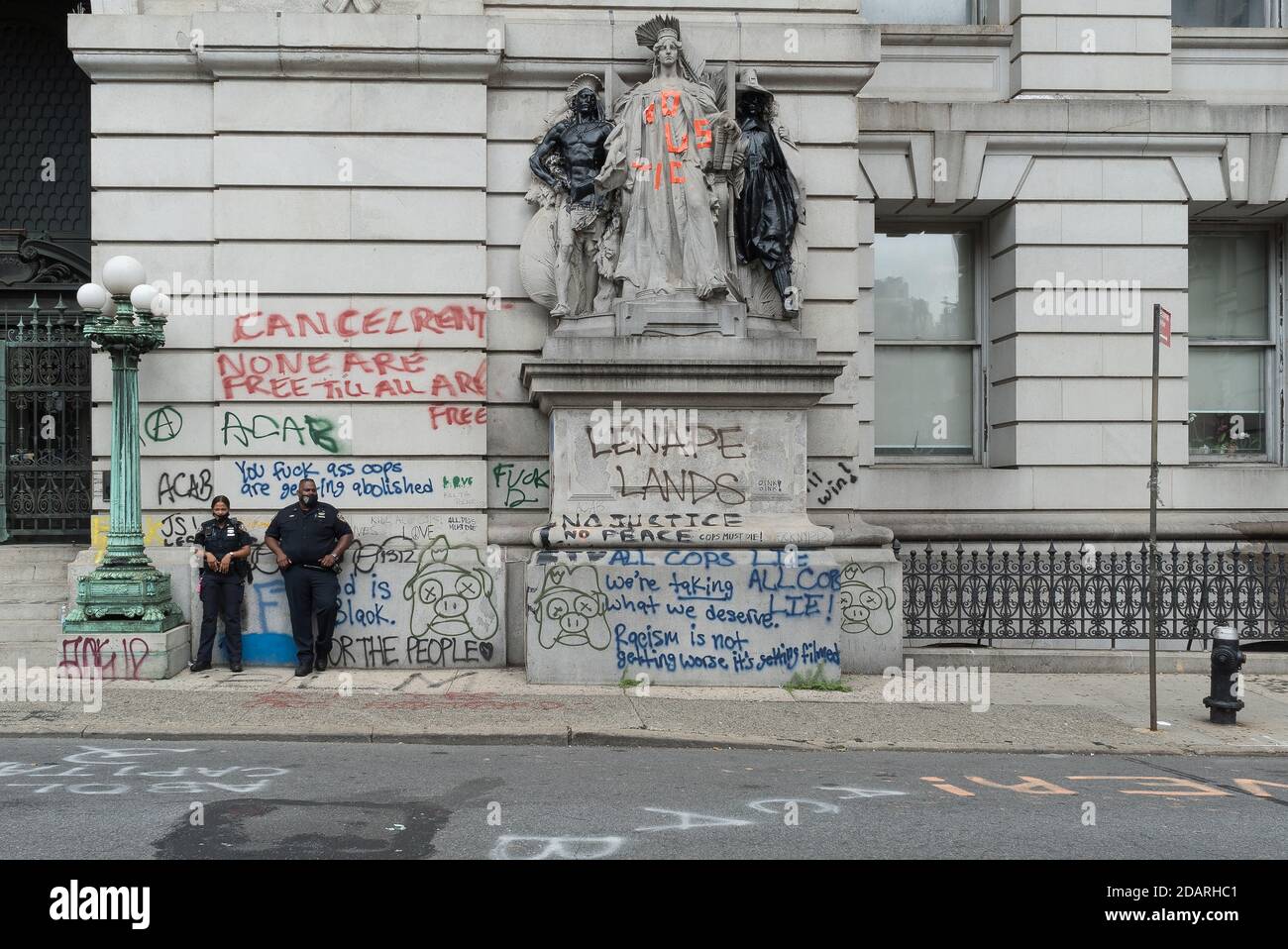 Due poliziotti che indossano una maschera stand presso l'ingresso della Sala surrogata dei primati accanto alla graffite e la statua vandalizzata di Philip Martiny. Foto Stock