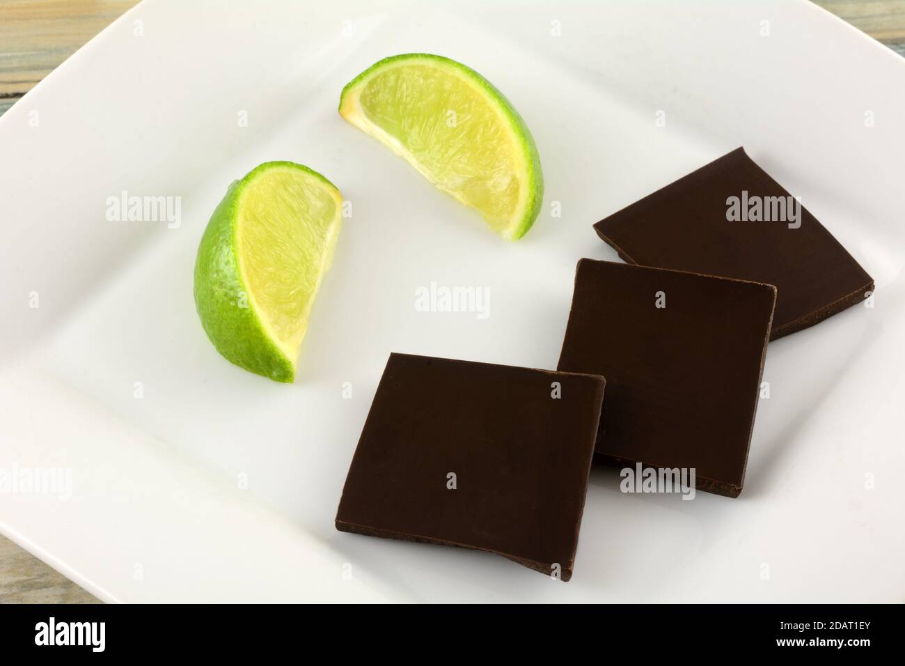 Pezzi da bar di cioccolato fondente al lime e menta con lime fresco cunei su piatto da dessert bianco Foto Stock