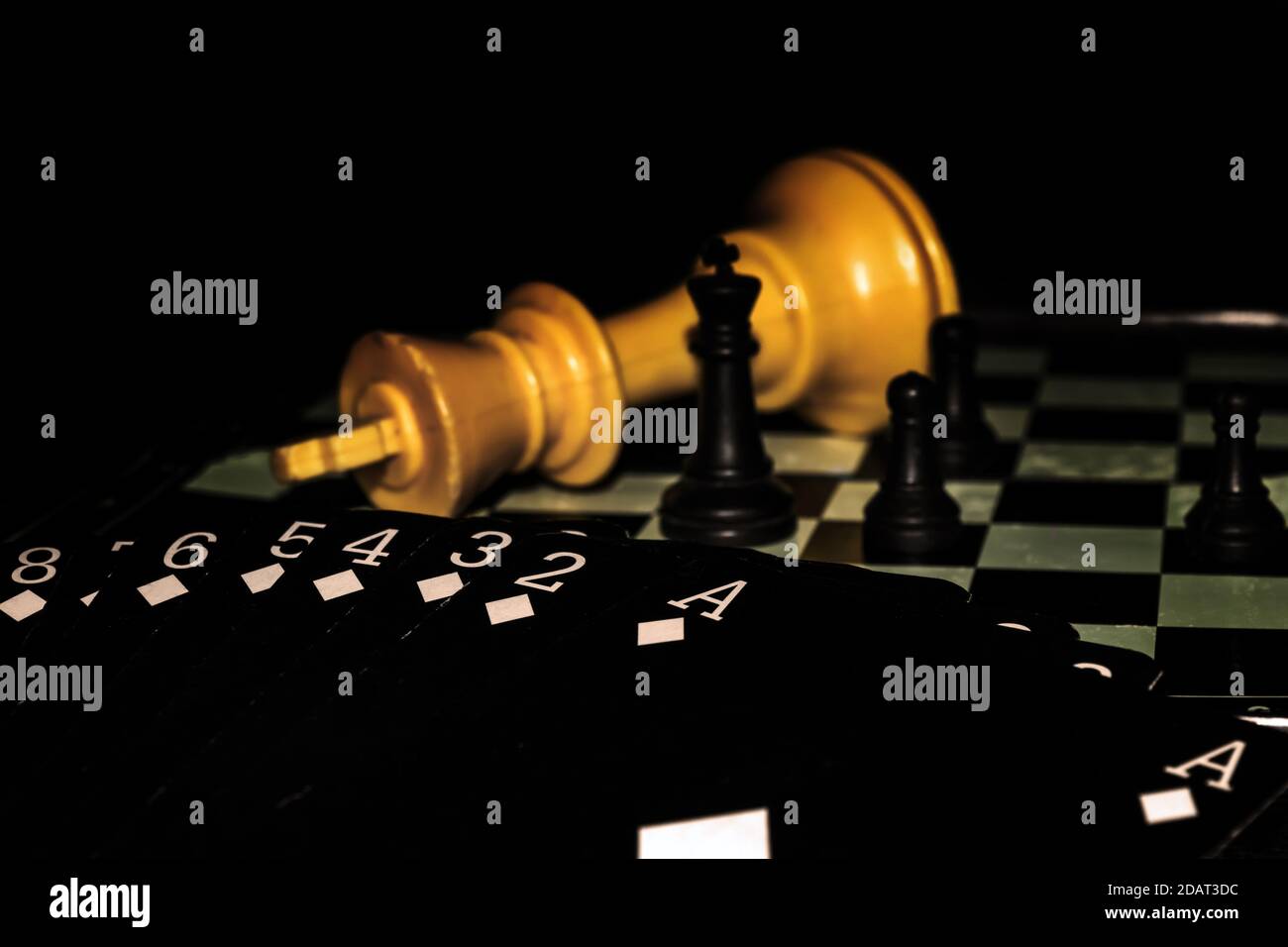 Mostra di un mazzo di carte nere che mostrano solo carte di diamante, su una scacchiera con quattro pezzi di scacchi in piedi e un grande re giallo sdraiato. Foto Stock
