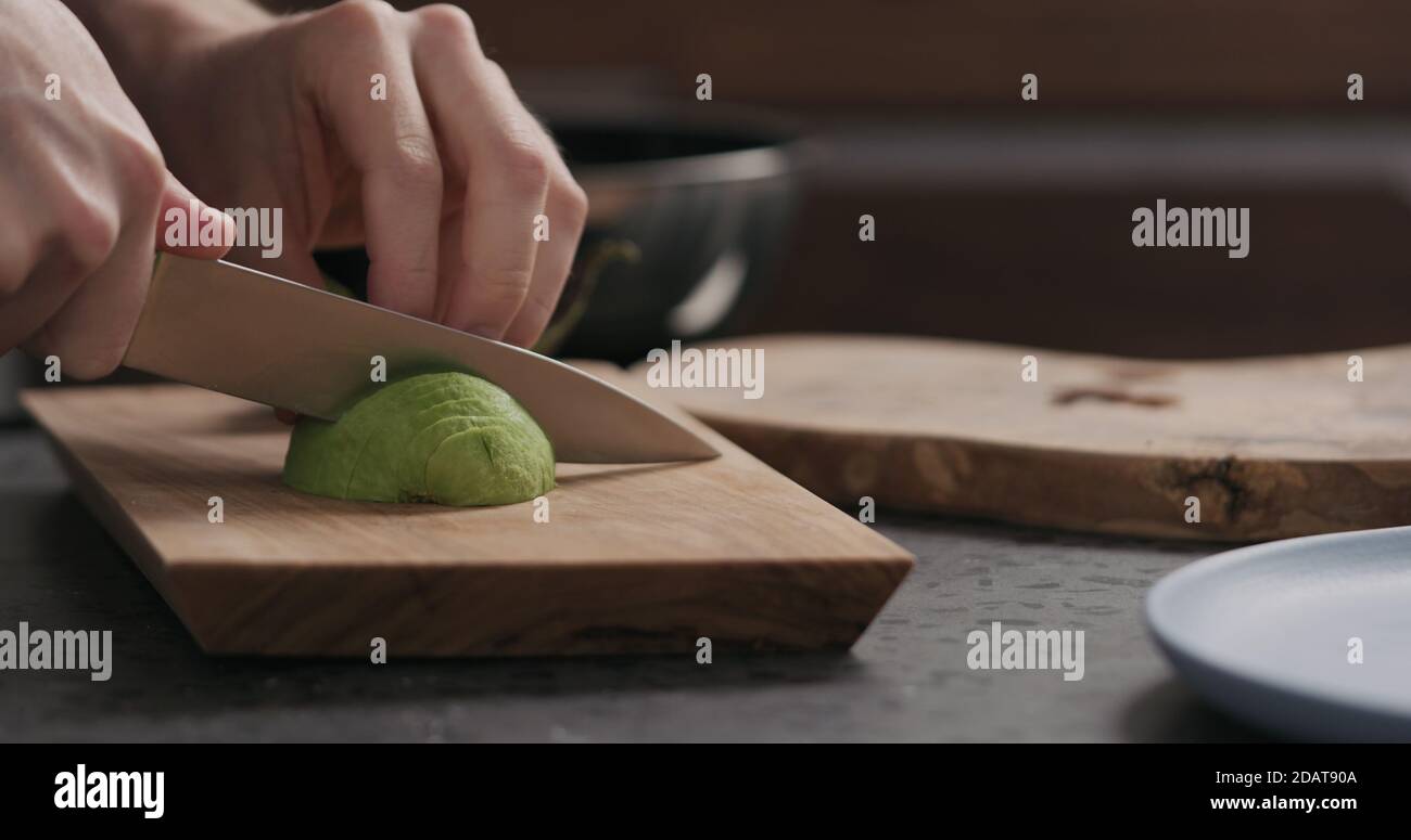 Uomo slow motion affettando avocado su tavola di ulivo, foto ampia Foto Stock