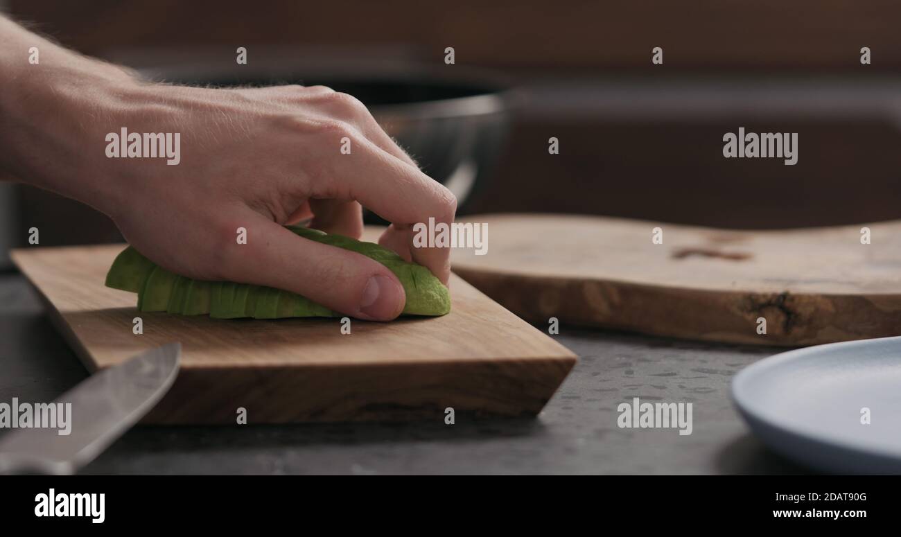 Uomo slow motion affettando avocado su tavola di ulivo, foto ampia Foto Stock