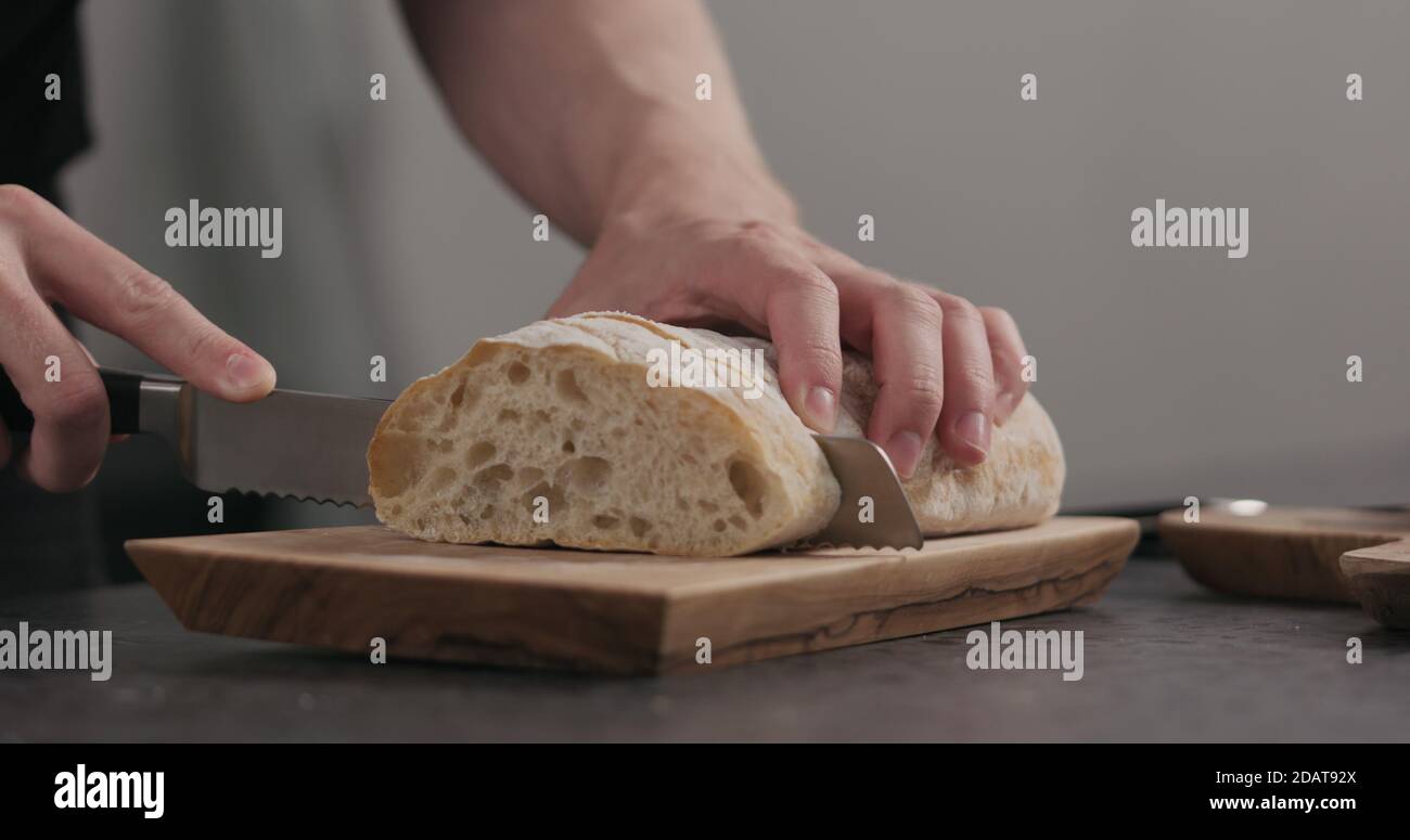 Uomo slow motion tagliando ciabatta con coltello per pane su tavola di olive, foto ampia Foto Stock
