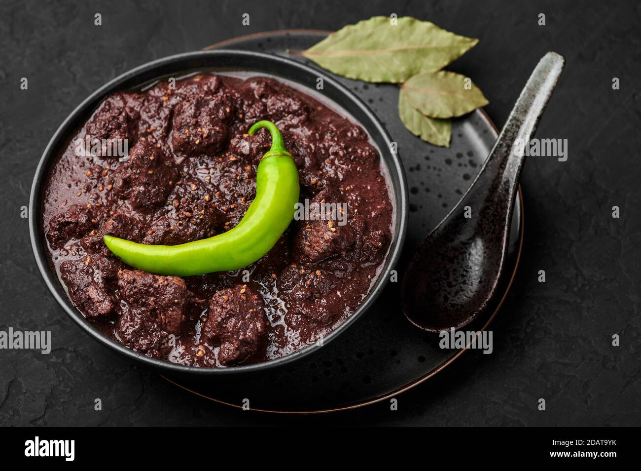 Dinuguan in ciotola nera su tavolo di ardesia scuro. Piccante cucina filippina maiale sangue stufato piatto con carne. Cibo asiatico. Foto Stock