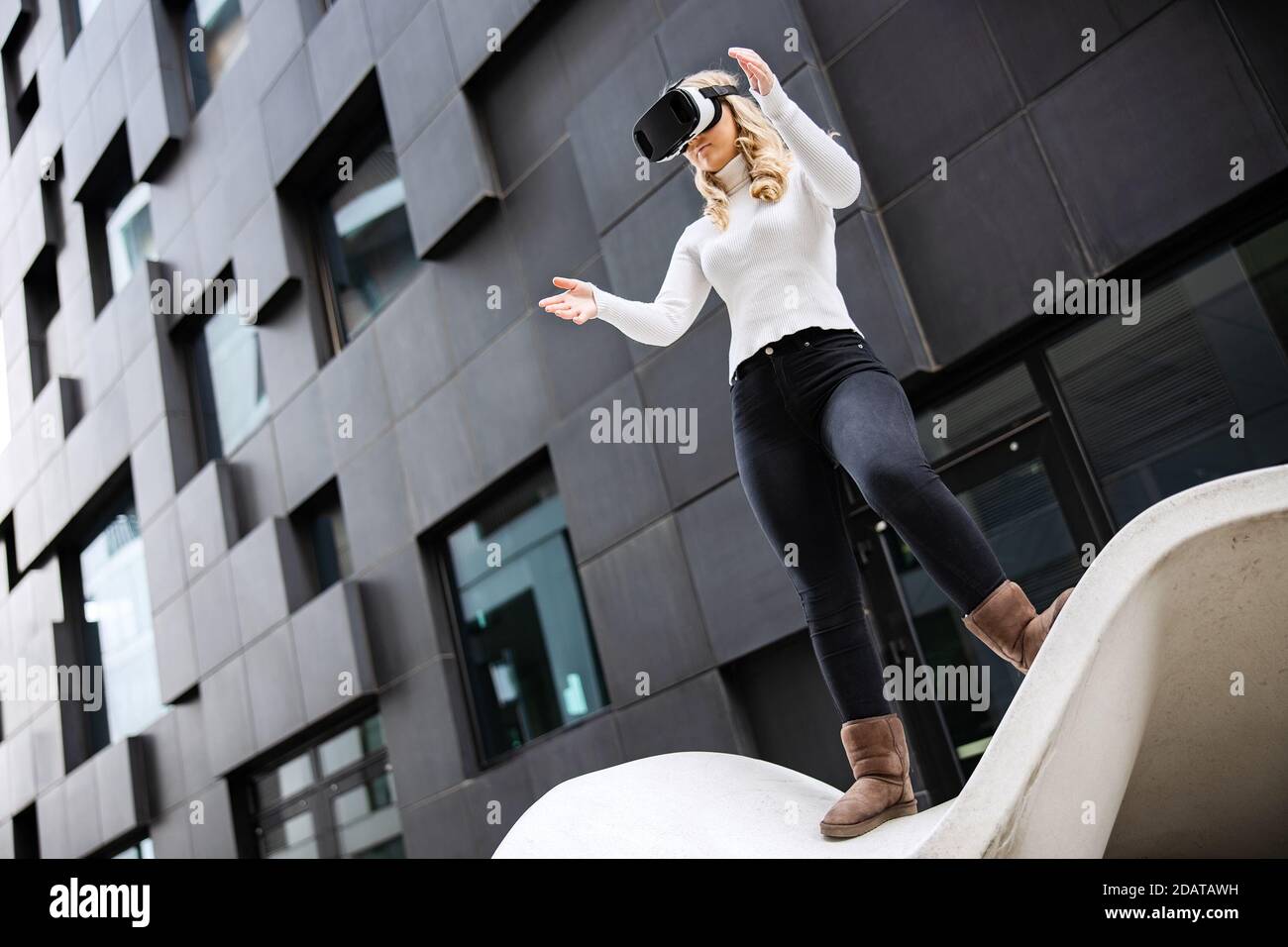 Giovane donna che indossa occhiali di realtà virtuale contro l'edificio futuristico Foto Stock