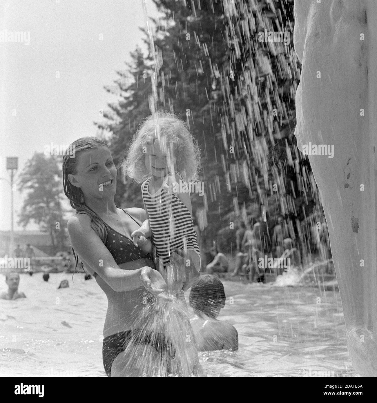 madre che tiene la figlia giovane sotto la fontana nella piscina pubblica 1970 ungheria Foto Stock