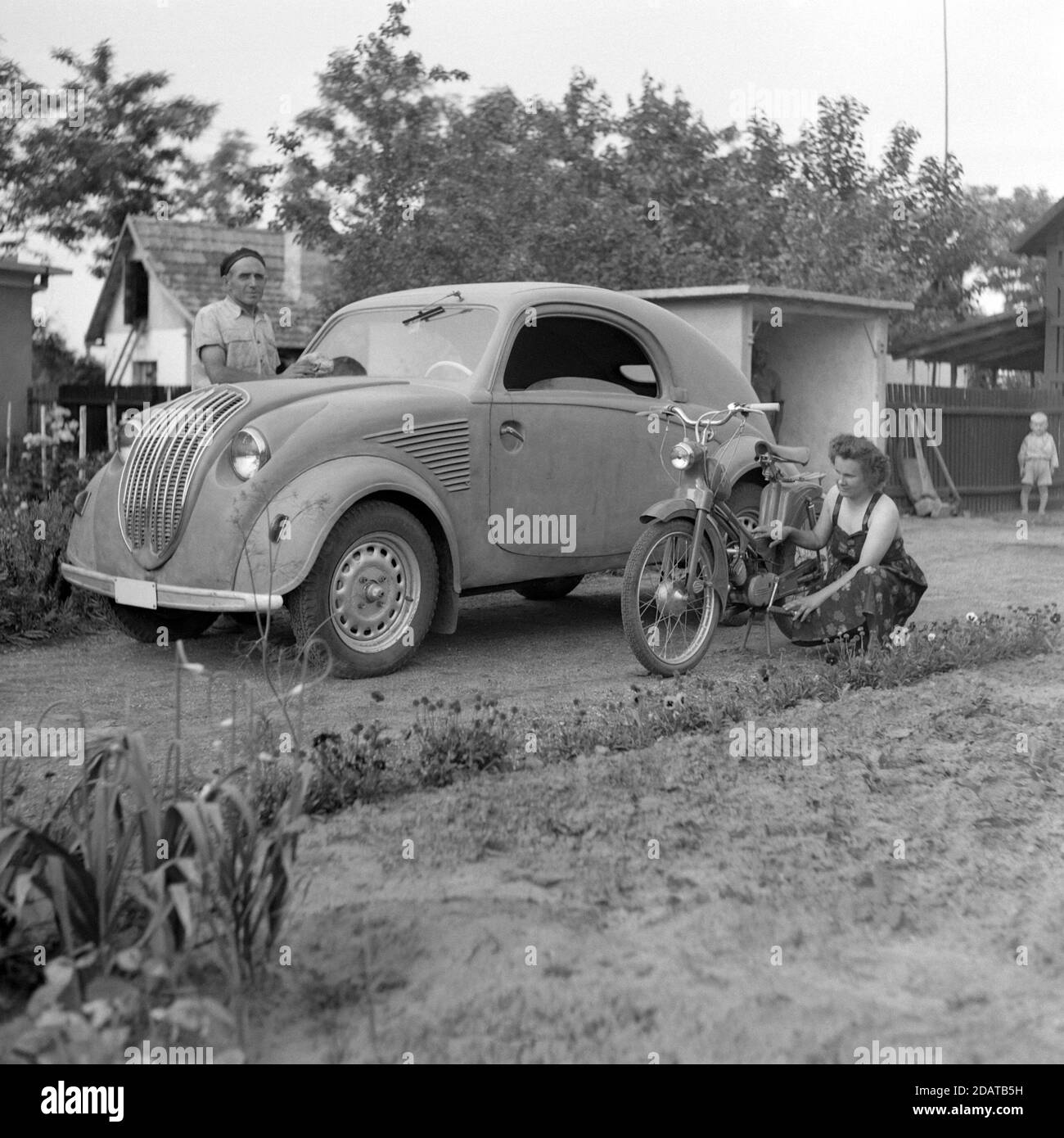 uomo che pulisce la sua auto steyr 55 mentre femmina assiste a. la sua berva ha ciclomentato nella loro casa 1950 ungheria Foto Stock
