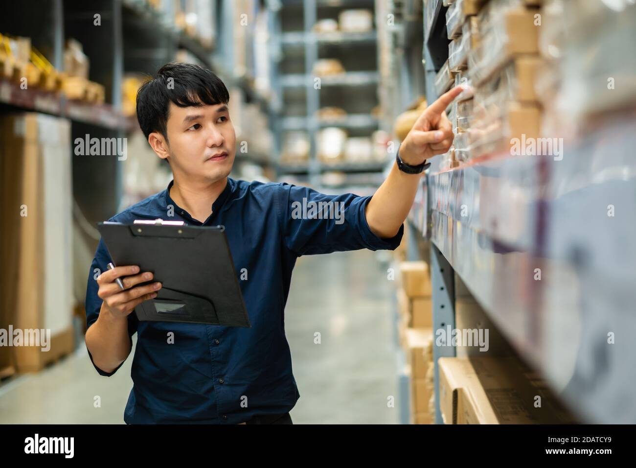 giovane uomo lavoratore tenere appunti e controllare l'inventario nel magazzino Foto Stock