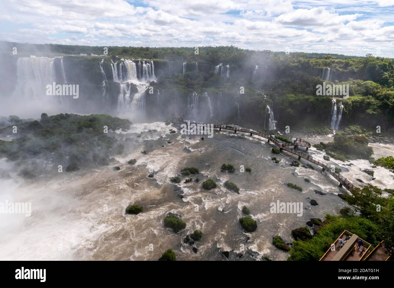 Una lunga passerella, piena di visitatori, che si estende attraverso le cascate di Iguazu nel Parco Nazionale, in Brasile. Sul lato opposto delle cascate in Argentina Foto Stock