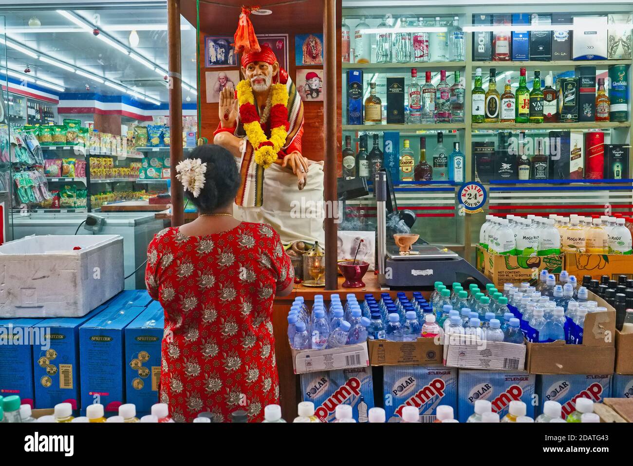 Una donna indù prega in un santuario a hindu saint Shirdi Sai Baba eretto in un supermercato di 24 ore accanto alla sezione dei liquori, Little India, Singapore Foto Stock