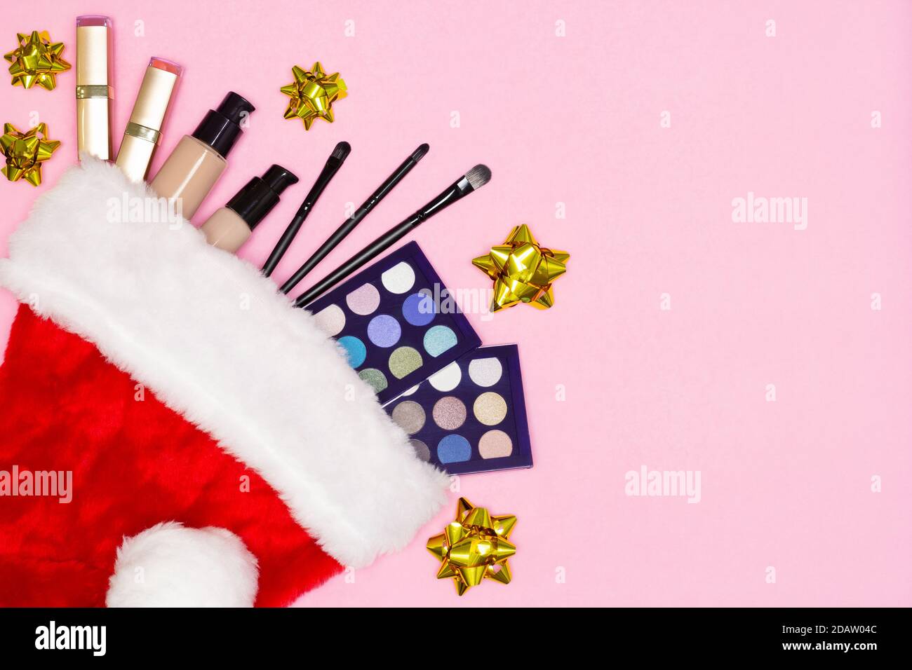 Set di prodotti per il trucco in cappello Santa con archi regalo lucido su sfondo rosa - vista dall'alto. Cosmetici di trucco come Natale e Capodanno presente concetto Foto Stock