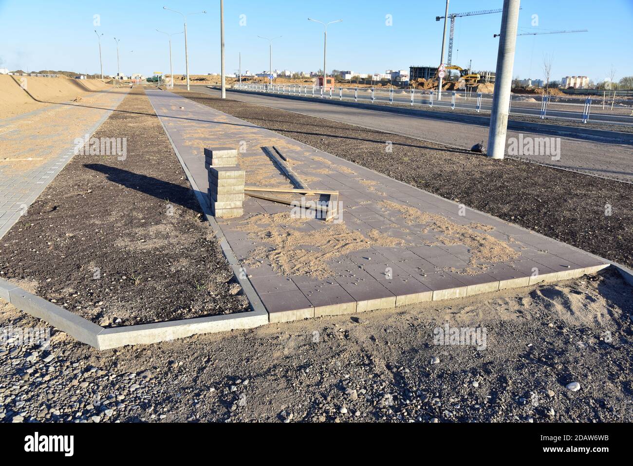 Posa di lastre e bordi di pavimentazione in cantiere. Processo di installazione di mattoni di pavimentazione nella zona pedonale della città. Spianatura della sabbia per il montaggio Foto Stock