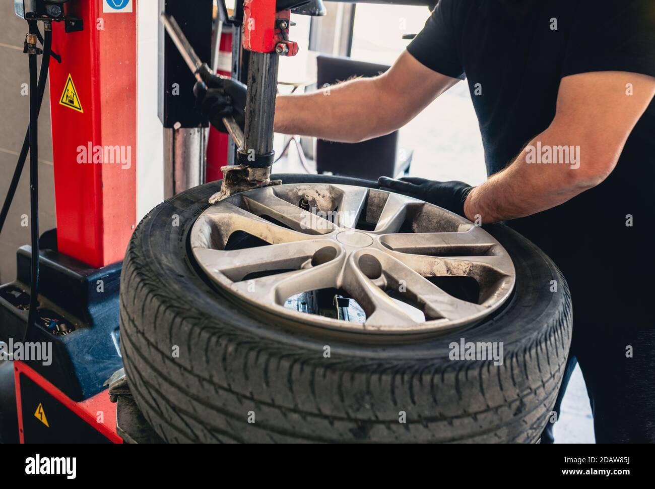 Meccanico con chiave pneumatica svita la ruota. Meccanico professionista maschile in un garage che fissa una ruota. Meccanico che ripara una ruota di automobile. Foto Stock