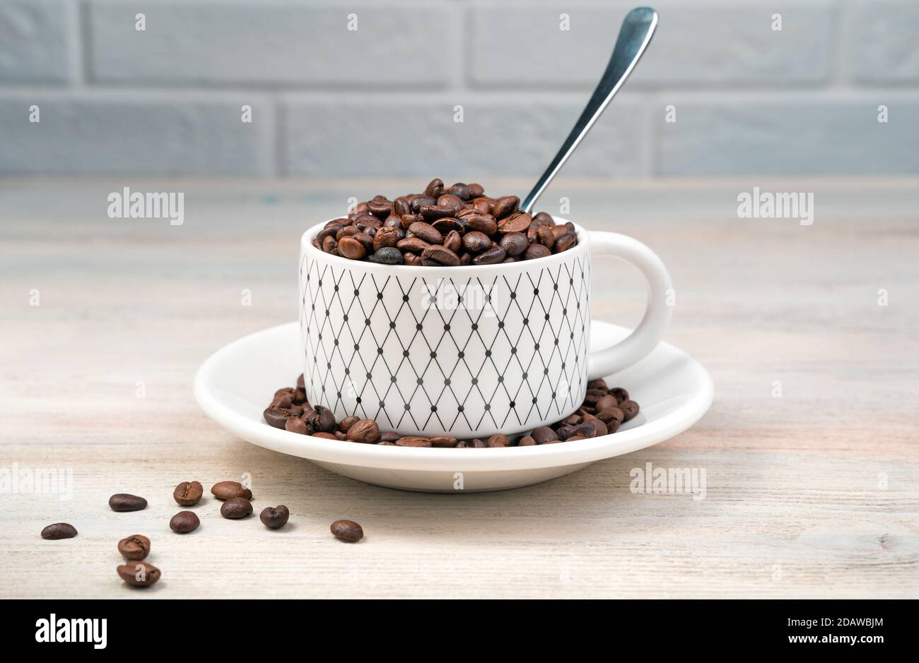 Tazza di caffè bianca piena di chicchi di caffè e un cucchiaio su uno sfondo chiaro. Foto Stock
