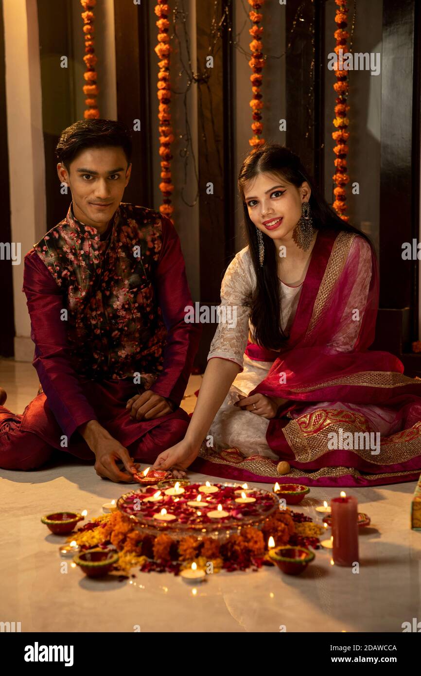 Ritratto di un uomo e di una donna indiani che illuminano diya e lampade in occasione delle feste di Diwali. Celebrazioni a casa. Foto Stock