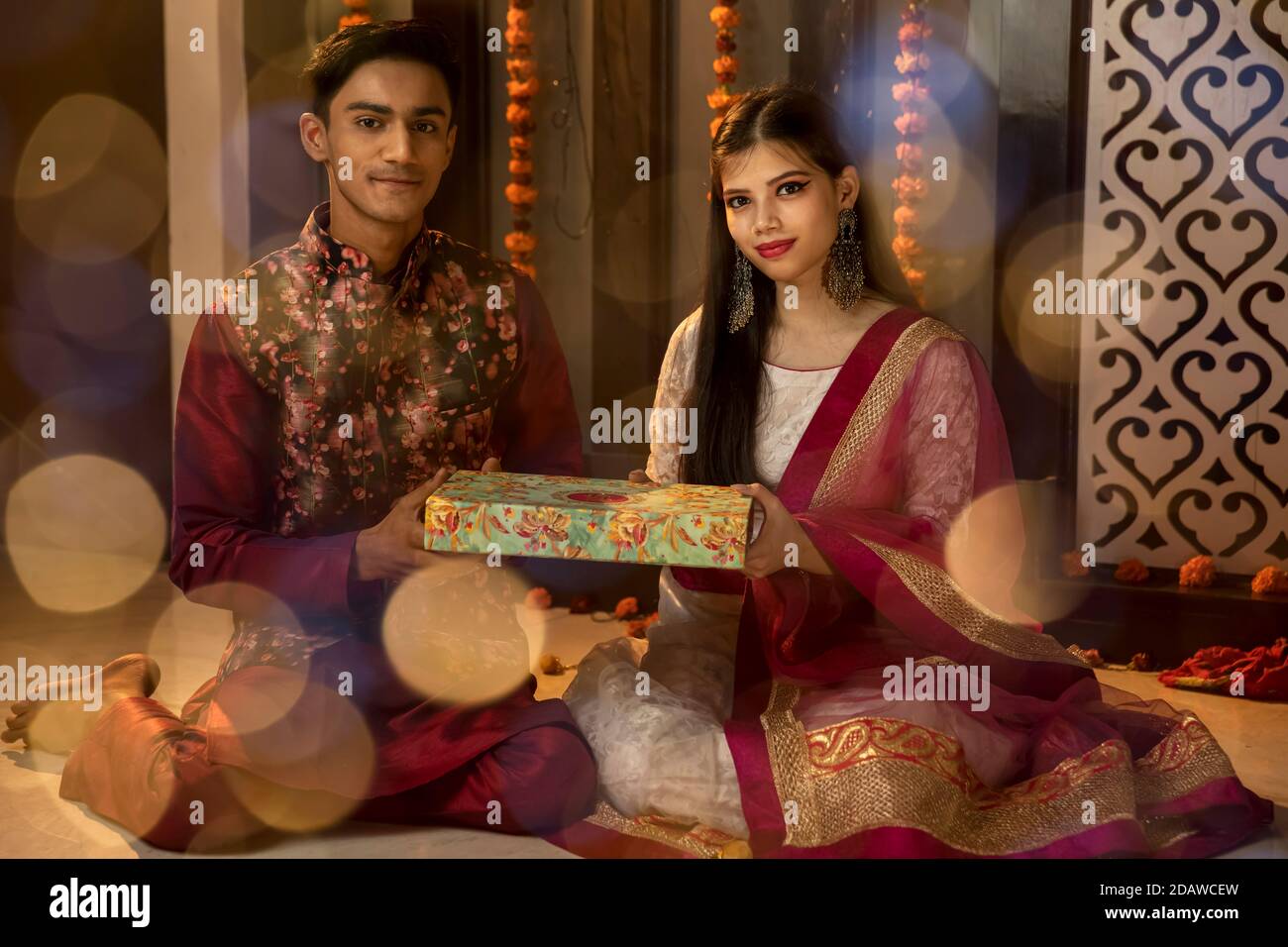 Ritratto di un uomo e di una donna indiani che illuminano diya e che tengono regali in occasione di festa di Diwali. Celebrazioni a casa. Foto Stock