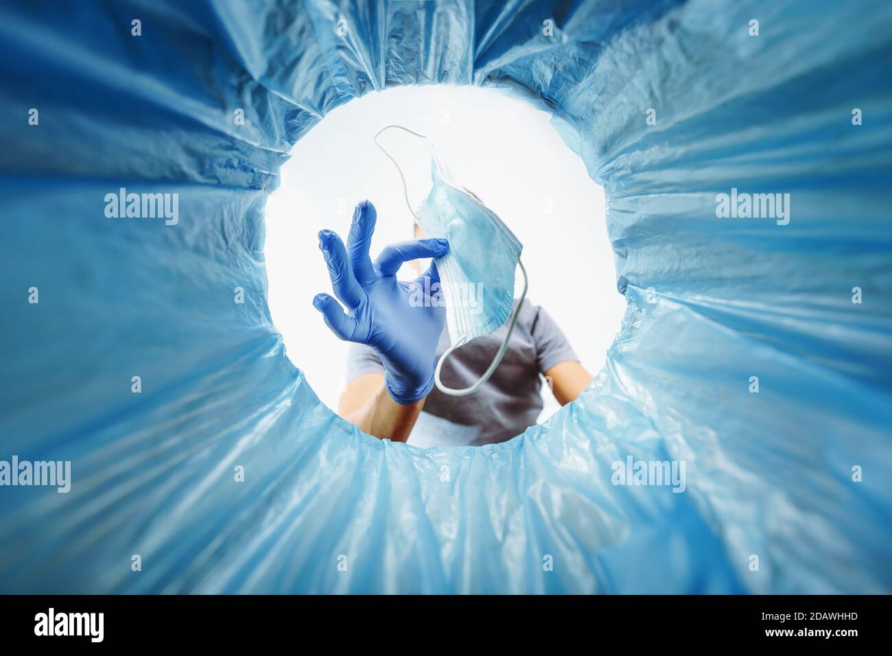 Un uomo dai guanti blu getta una maschera medica usata nel cestino, una vista dal secchio. Foto Stock