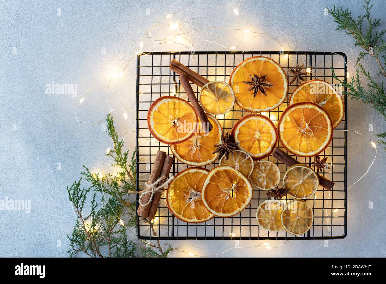 Arance secche, limoni, bastoni di cannella e stelle di anice su uno sfondo di luci di Natale e rami di abete. Foto Stock