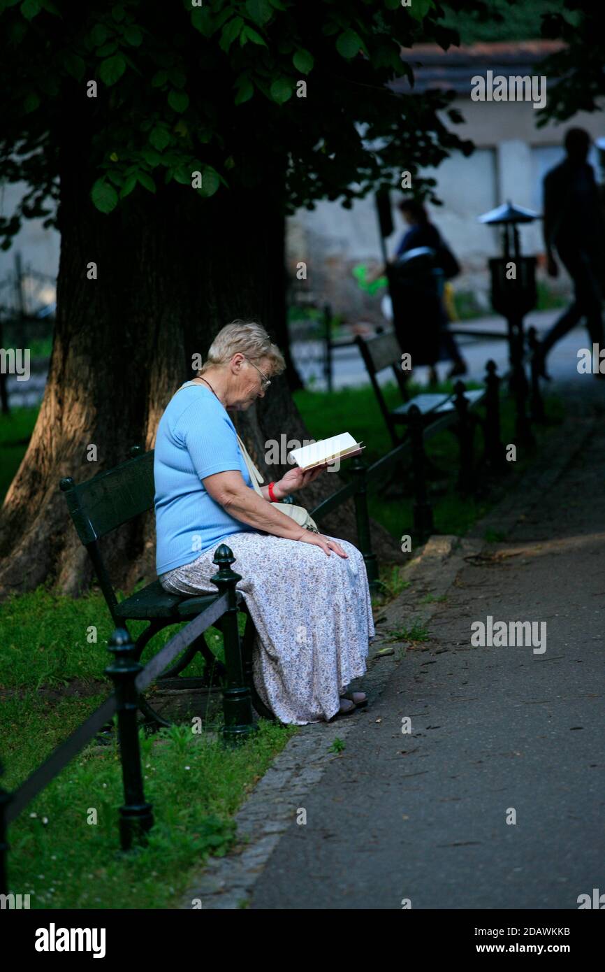 Una donna anziana è seduta su una panchina e sta leggendo Un libro in Planty Park nel centro di Cracovia Foto Stock