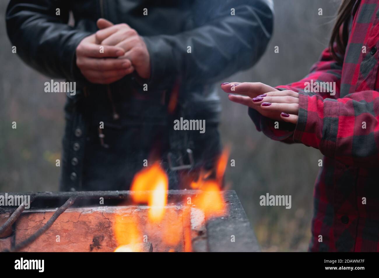 Mani di due persone che si riscaldano da un fuoco all'aperto. Crogiolandosi dal fuoco nella strada, l'uomo e la donna ottengono conforto dalla luce Foto Stock