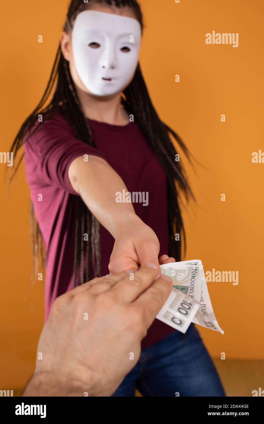 La mano maschile prende denaro da uno straniero che ha una maschera in tutto il suo volto in modo che nessuno lo riconosca. Denaro promesso in un prestito anonimo. Foto Stock