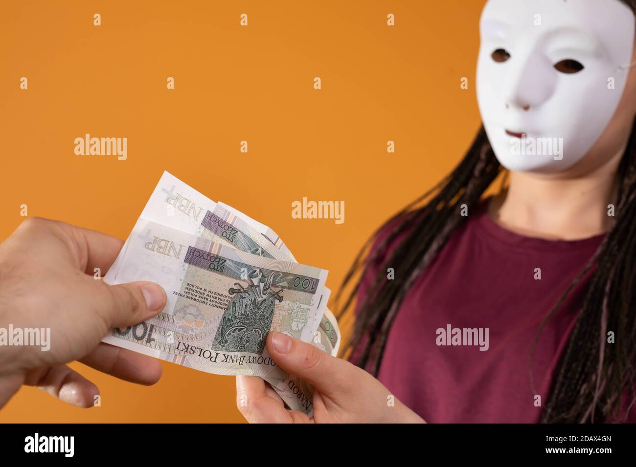 La mano maschile prende denaro da uno straniero che ha una maschera in tutto il suo volto in modo che nessuno lo riconosca. Denaro promesso in un prestito anonimo. Foto Stock
