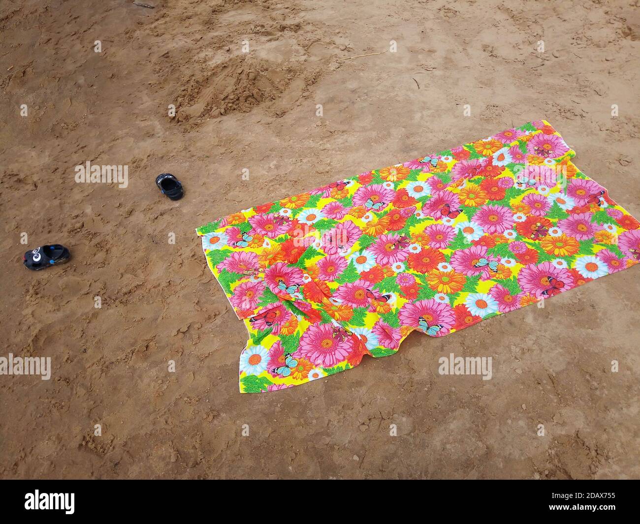 Telo da spiaggia multicolore e pantofole per bambini sulla sabbia bagnata. Foto Stock