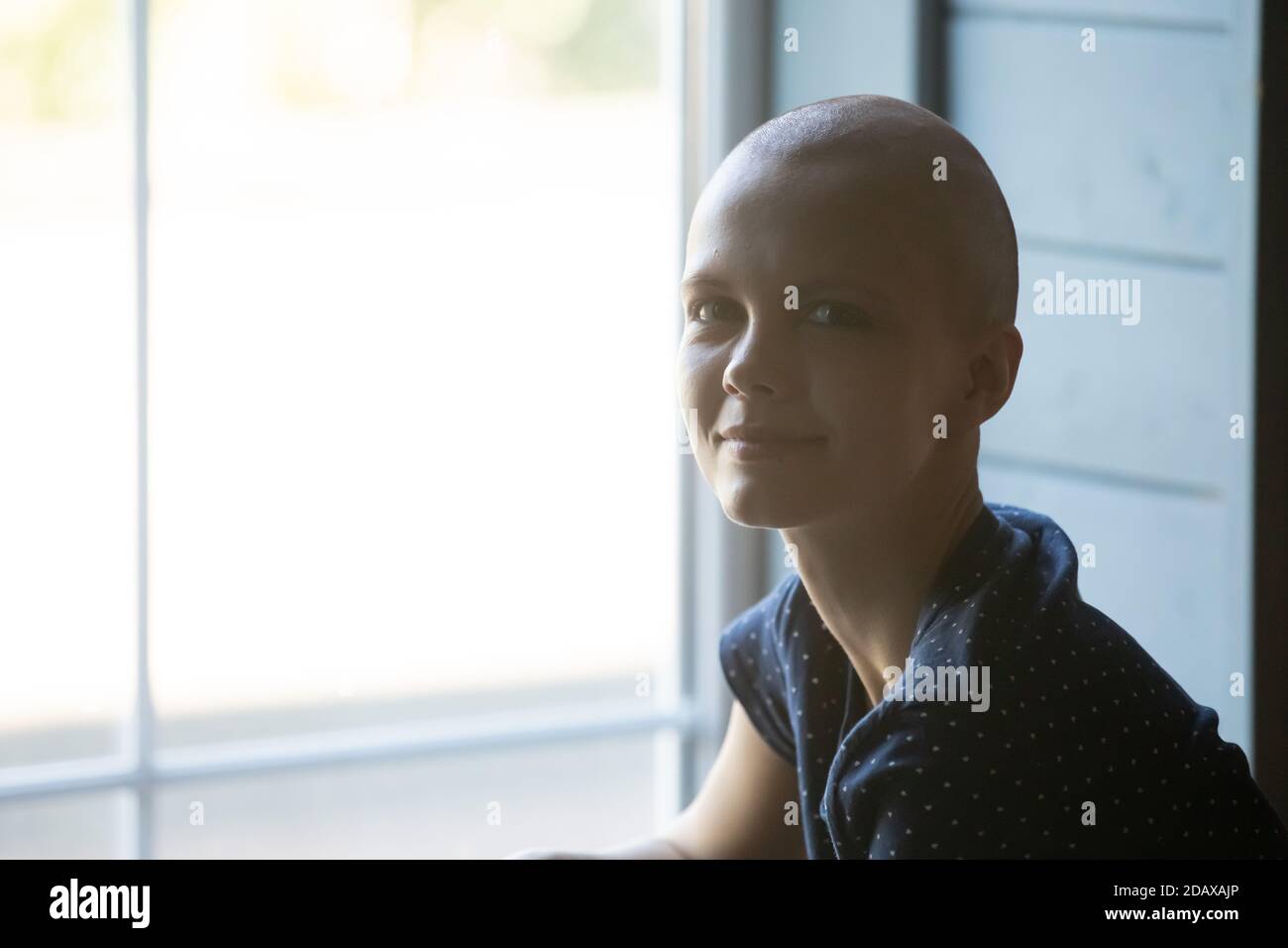 Calma sorridente giovane donna che riceve il trattamento del cancro seduto vicino alla finestra Foto Stock