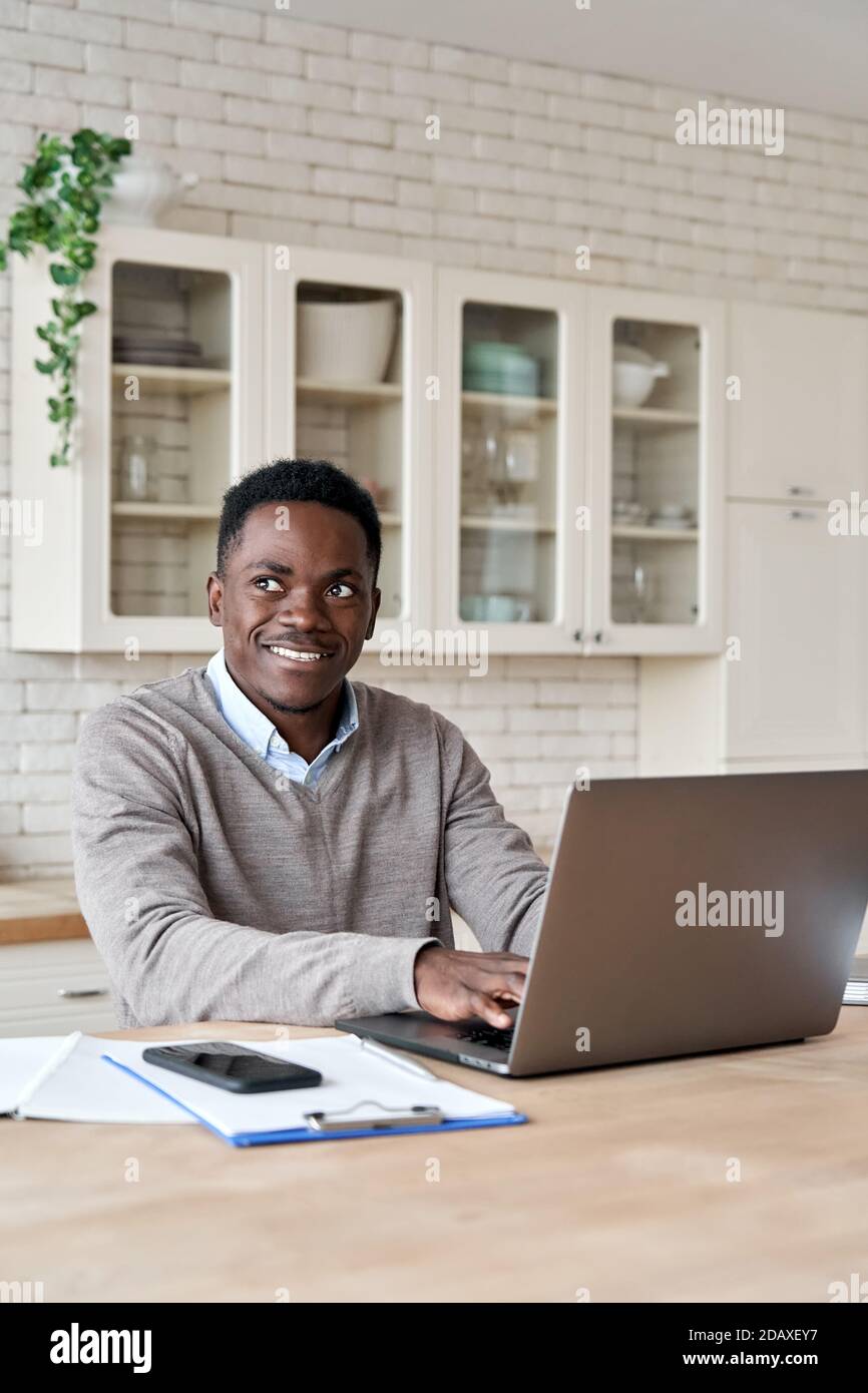 Sorridente afroamericano che usa un computer portatile che lavora da casa, verticale. Foto Stock