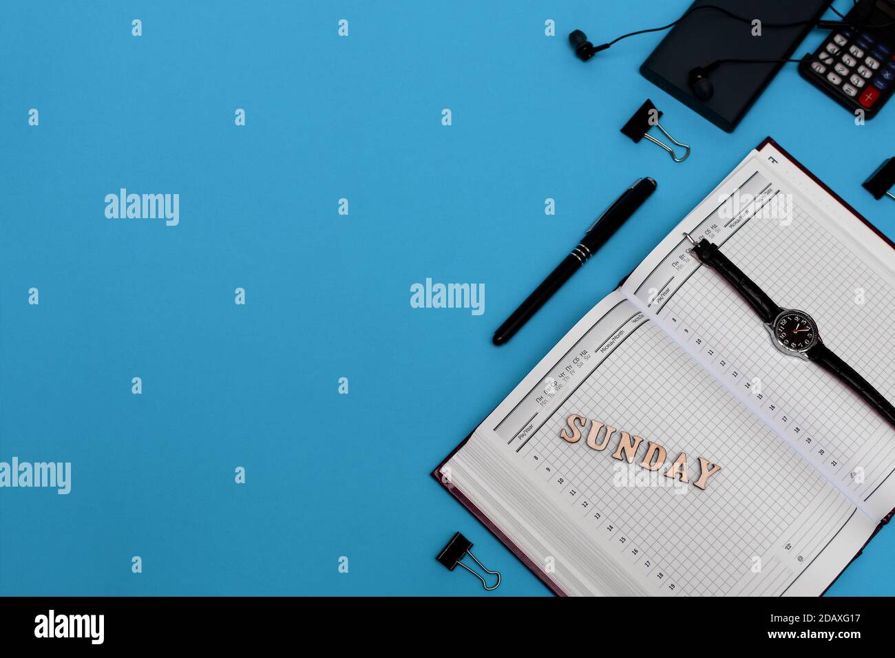 Moderna scrivania da ufficio con notebook, penna e materiali di consumo vuoti. Copiare lo spazio su sfondo blu. Vista dall'alto. Stile di posa piatto. Iscrizione domenica Foto Stock