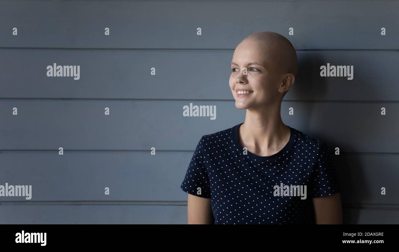 Donna sorridente paziente cancro in piedi vicino parete grigia esprimendo coraggio Foto Stock