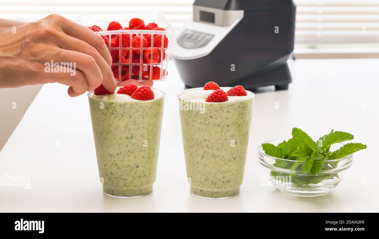 Frullato di banana al sedano con semi di Chia e miele in bicchieri, servito con lamponi freschi e foglie di menta, primo piano sul tavolo da cucina. Colazione sana Foto Stock