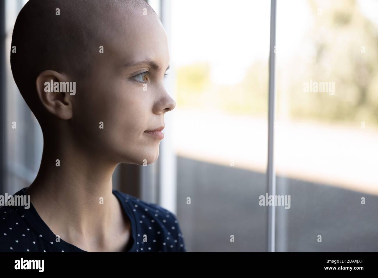 Giovane donna concentrata che riceve il trattamento del cancro in piedi vicino alla finestra Foto Stock